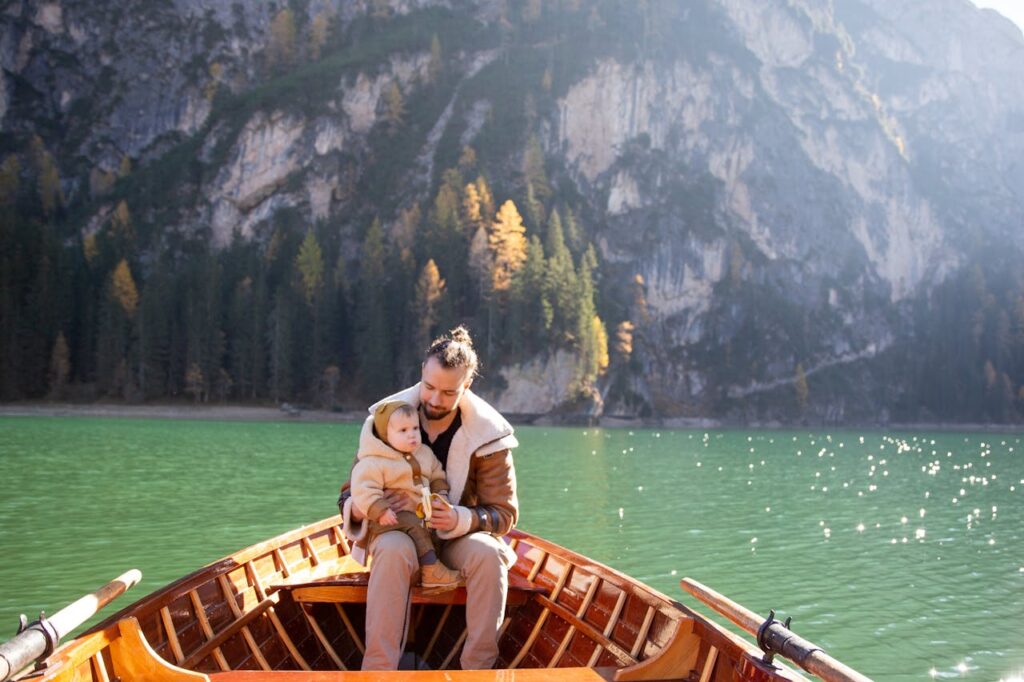 Man in Brown Jacket Sitting on Brown Wooden Boat on Lake